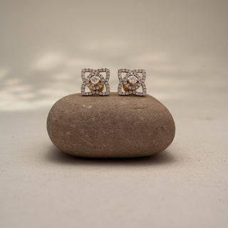 Front view of geometric diamond stud earrings in 14KT Yellow Gold, featuring a round lab-grown diamond framed by pavé-set diamond loops. Displayed on a stone surface, highlighting intricate brilliance.