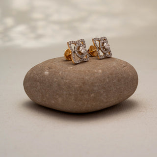Side view of geometric diamond stud earrings in 14KT Yellow Gold, featuring a round lab-grown diamond framed by pavé-set diamond loops. Displayed on a stone surface, highlighting intricate brilliance.