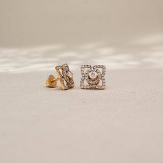 Angled view of geometric diamond stud earrings in 14KT Yellow Gold, featuring a round lab-grown diamond framed by pavé-set diamond loops. Displayed on a beige backdrop, highlighting intricate brilliance.