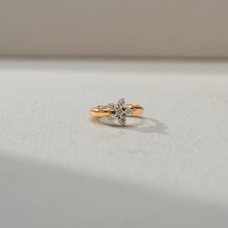 Top view of a petite gold hoop earring featuring a floral diamond cluster centerpiece, showcased on a neutral surface with soft natural lighting and a delicate shadow.