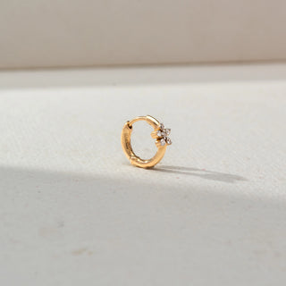 Side view of a petite gold hoop earring featuring a floral diamond cluster accent, showcased on a neutral surface with soft natural lighting and a delicate shadow.