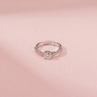 Top view of a 14KT white gold ring featuring a round-cut diamond in a criss-cross design, set against a pink background.