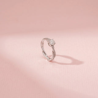 Angled view of a 14KT white gold ring featuring a round-cut diamond in a criss-cross design, set against a pink background.