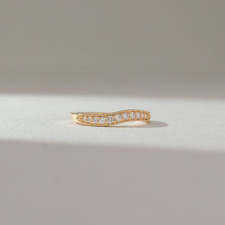 Front view of diamond band ring in yellow gold, featuring a flowing wave design set with round lab-grown diamonds along the centre. Set on a soft neutral backdrop, it reflects smooth curves and subtle brilliance.
