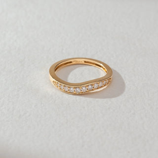 Top view of diamond band ring in yellow gold, featuring a smooth curved design set with round lab-grown diamonds along the centre. Set on a soft neutral surface, it reflects minimal elegance and refined sparkle.