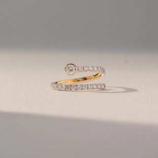 Front view of Open Wrap Diamond Ring in 14KT Yellow Gold, featuring a bezel-set round lab grown diamond with a pavé band. Set on a beige backdrop, the design highlights layered sparkle and modern elegance.
