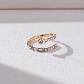 Top view of Open Wrap Diamond Ring in 14KT Yellow Gold, featuring a bezel-set round lab grown diamond with a pavé band. Set on a beige backdrop, the design highlights symmetry and refined elegance.
