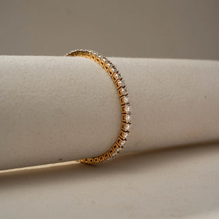 Side view of a classic gold tennis bracelet showcasing round brilliant gemstones in elevated prong settings, wrapped around a soft neutral cylindrical display stand.