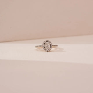 Front view of Reia’s 18 KT Yellow Gold Oval Halo Diamond Engagement Ring. Captured against a cream backdrop, the layout highlights the brilliant oval centre stone and pavé-set shoulders.