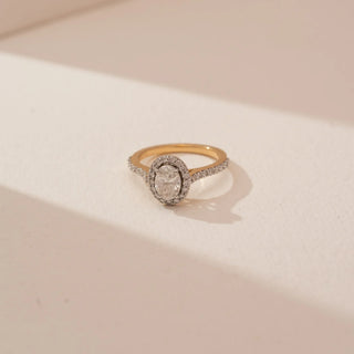Angled top view of Reia’s 18 KT Yellow Gold Oval Halo Diamond Engagement Ring, showing the pavé-set band. Captured against a cream backdrop, the layout highlights the majestic and radiant silhouette.