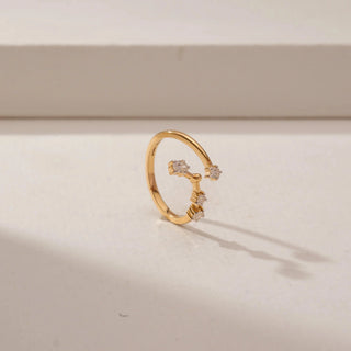 Angled view of an open diamond ring in 14KT Yellow Gold, featuring floral diamond clusters along a curved band against a beige backdrop.