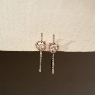 Front view of diamond drop earrings in 14 KT Rose Gold, featuring heart-inspired pavé diamond motifs with floating center diamonds and sleek linear diamond accents against a neutral backdrop.
