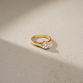  Top view of a round solitaire engagement ring in 14 KT Yellow Gold, featuring a round lab-grown diamond in a classic six-prong setting on a polished gold band, displayed against a beige backdrop.