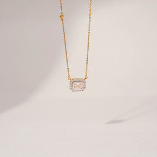 Close up view of an emerald-cut lab-grown diamond pendant necklace in 18KT Yellow Gold, featuring a bezel-set emerald-cut centre stone with a sparkling diamond halo. Captured against a beige backdrop, the elegant design radiates brilliance.
