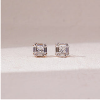Front view of square halo diamond stud earrings in white gold, featuring a centred princess-cut lab-grown diamond framed by baguette and round stones. Placed on a soft beige surface, the design reflects structured brilliance.
