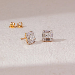 Top view of square halo diamond stud earrings in yellow gold, featuring centred princess-cut lab-grown diamonds framed by baguette and round stones. Placed on a textured beige surface, the design casts a soft shadow.
