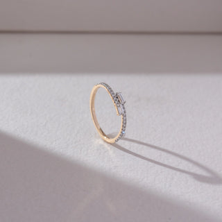 Side angled view of baguette diamond band ring in yellow gold, featuring twin baguette-cut lab-grown diamonds at the centre with a row of round diamonds along the band. Set on a soft neutral backdrop, it highlights sleek form and sparkle.