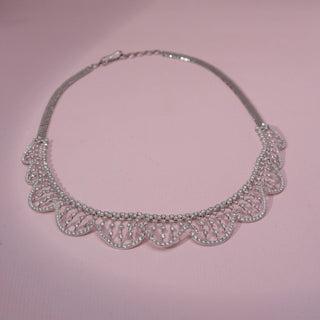 Top view of a wave-inspired lab-grown diamond necklace in 14KT White Gold, featuring cascading diamond drop accents. Captured against a pink backdrop, the graceful openwork design radiates elegance.