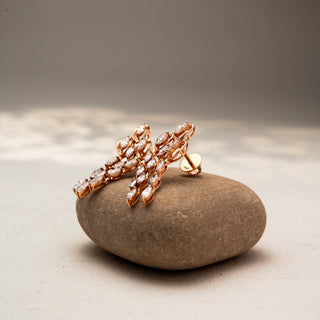 Side view of cascading diamond drop earrings in 14 KT Rose Gold, featuring marquise-cut diamonds in layered leaf-inspired motifs, displayed on a textured stone surface.
