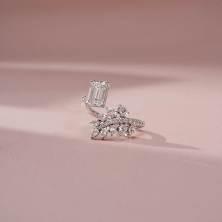 Front view of a white gold diamond ring featuring an emerald-cut center stone and a marquise diamond leaf motif with pavé accents, displayed on a soft pink background.