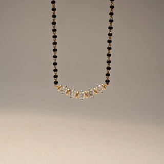 Close Up  view of a diamond mangalsutra necklace in 14 KT Yellow Gold, featuring five round diamonds set in a graceful curved arrangement along a black beaded chain against a neutral backdrop.
