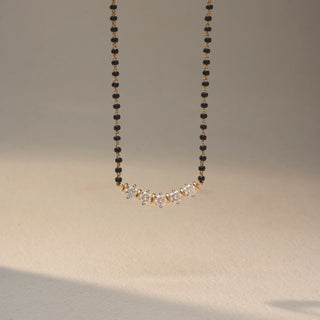 Front view of a diamond mangalsutra necklace in 14 KT Yellow Gold, featuring five round diamonds set in a graceful curved arrangement along a black beaded chain against a neutral backdrop.
