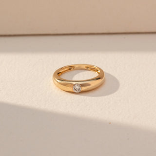 Top view of Flush Set Diamond Band Ring in 14KT Yellow Gold, featuring a single round lab grown diamond embedded in a smooth band. Set on a beige backdrop, the design highlights clean minimal elegance.
