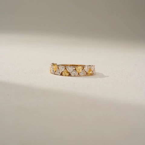 Front view of a diamond eternity band in 14 KT Yellow Gold, featuring alternating heart-shaped yellow and white lab-grown diamonds in a continuous shared-prong design, displayed against a beige backdrop.