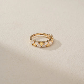 Side front view of a diamond eternity band in 14 KT Yellow Gold, featuring alternating heart-shaped yellow and white lab-grown diamonds in a shared-prong design, displayed against a beige backdrop.