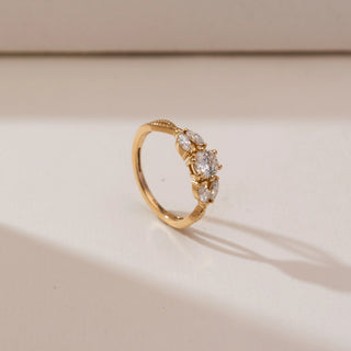 Angled view of Radiant Twisted Gold Diamond Ring in yellow gold, featuring a round lab-grown diamond with marquise diamond accents set on a textured twisted band, displayed on a soft beige backdrop.