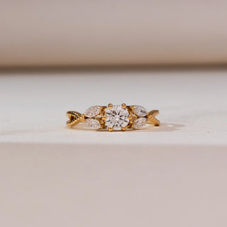 Front view of Radiant Twisted Gold Diamond Ring in yellow gold, featuring a round lab-grown diamond flanked by marquise diamond accents on a textured twisted band, displayed on a soft beige surface.