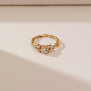 Top view of Radiant Twisted Gold Diamond Ring in yellow gold, featuring a round lab-grown diamond with marquise diamond accents set on a textured twisted band, displayed on a soft beige backdrop.