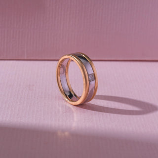 Angled side view of a two-tone band ring featuring a flush-set princess-cut lab-grown diamond. Captured against a soft pink backdrop, the sleek contemporary design highlights minimalist elegance and refined brilliance.
