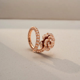 Angled view of a floral diamond statement ring in 14 KT Rose Gold, featuring a rose-inspired cluster of round lab-grown diamonds and a diamond-accented split shank, displayed against a beige backdrop.