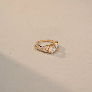 Side view of a round diamond engagement ring in 14 KT Yellow Gold, featuring a round lab-grown diamond accented by marquise-shaped and pavé-set diamonds in a nature-inspired band, displayed against a beige backdrop.