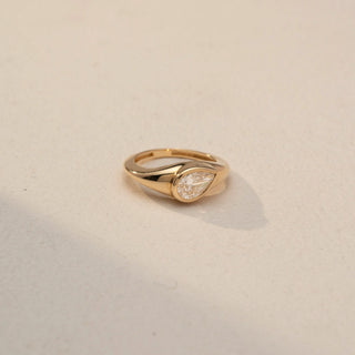 Top view of a pear-cut solitaire signet ring in 14 KT Yellow Gold, featuring a bezel-set pear-shaped lab-grown diamond in a sleek tapered band, displayed against a beige backdrop.