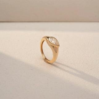 Angled view of a pear-cut solitaire signet ring in 14 KT Yellow Gold, featuring a bezel-set pear-shaped lab-grown diamond in a sleek tapered band, displayed against a beige backdrop.