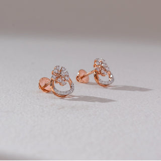 Angled back view of floral diamond stud earrings in rose gold, showing screw backs with pear-shaped lab-grown diamonds in a blooming cluster above a curved diamond-studded base. Set on a soft neutral surface, they highlight detail.