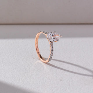 Side view of Pear Solitaire Diamond Ring in 14KT Rose Gold, featuring a centred pear-shaped lab grown diamond with a pavé-set band. Set on a beige backdrop, the design highlights depth and elegance.

