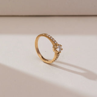 Angled side view of Modern Collet Pavé Diamond Ring in yellow gold, showcasing a round lab-grown diamond in a collet setting with pavé diamond accents along the band, placed on a soft beige backdrop.