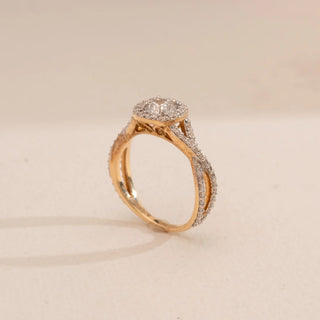 Side view of Reia’s 14 KT Yellow Gold Elegant Twisted Halo Diamond Ring. It highlights the round-cut central diamond, shimmering halo, and fluid, pavé-set twisted band on a cream backdrop.