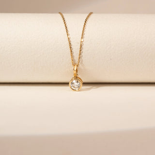 Close up view of a 14KT Yellow Gold diamond pendant with a round bezel-set centre diamond and a simple bail.
