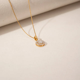 Top view of a halo diamond pendant in 14KT Yellow Gold, featuring a round centre diamond surrounded by smaller stones against a beige backdrop.
