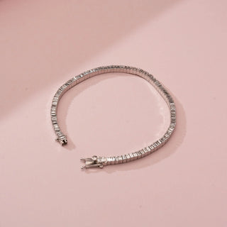 Top-down view of Reia’s 14 KT White Gold Elegant Line Baguette Diamond Bracelet. It features a continuous row of sleek baguette-cut diamonds with a secure clasp on a soft pink backdrop.