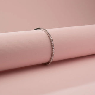 Angled view of Reia’s 14 KT White Gold Elegant Line Baguette Diamond Bracelet. It showcases the continuous line of baguette-cut diamonds on a soft pink cylindrical display.