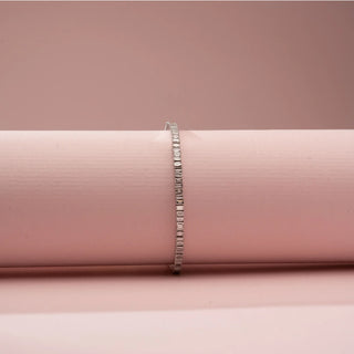 Front view of Reia’s 14 KT White Gold Elegant Line Baguette Diamond Bracelet. It showcases a continuous line of baguette-cut diamonds wrapped around a soft pink cylinder on a pink backdrop.