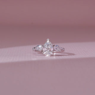 Front view of pear diamond ring in white gold, featuring a centred pear-shaped lab-grown diamond with matching side stones on a pavé band. Placed on a soft pink surface, the design reflects radiant brilliance.
