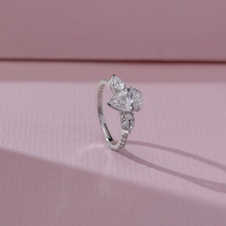 Side view of pear diamond ring in white gold, featuring a centred pear-shaped lab-grown diamond with matching side stones on a pavé band. Placed on a soft pink surface, the design casts a soft shadow.
