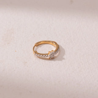 Top view of a gold nose ring, featuring pavé-set diamonds with a floral diamond accent at the center. Captured against a soft beige backdrop, the design reflects delicate sparkle and elegance.