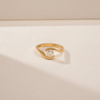Close-up view of a 14KT Yellow Gold diamond ring with a round centre stone and flowing crossover band.